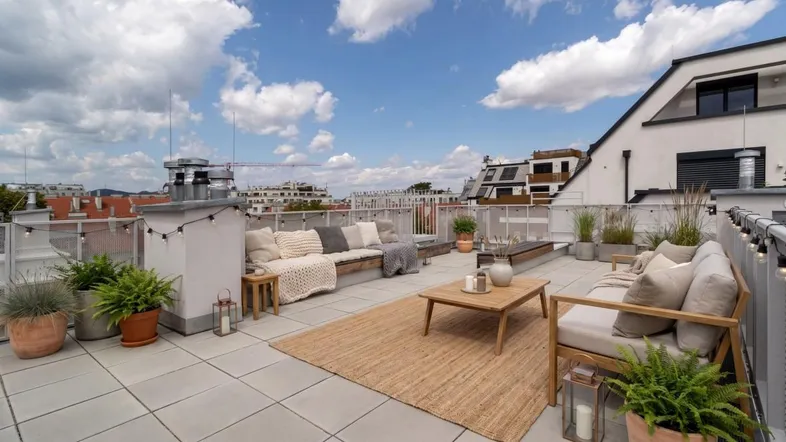 Geräumige Dachterrasse mit bequemen Loungemöbeln, Pflanzen und Blick auf die Stadt.