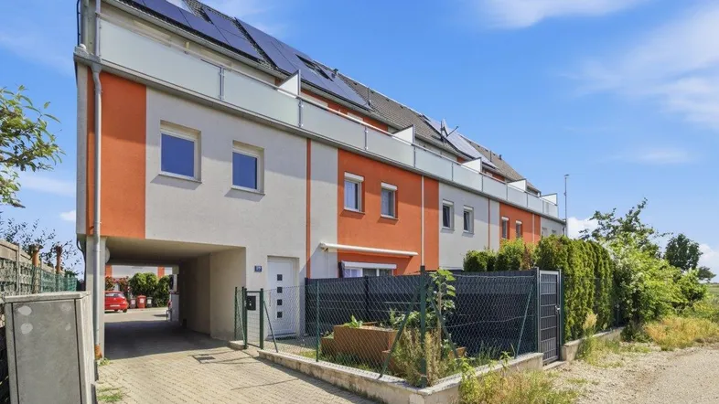 Moderne Reihenhäuser mit orangefarbenen Akzenten, Solarpaneelen auf dem Dach und Carport-Einfahrt.