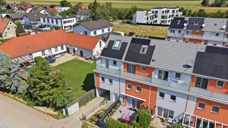 Luftaufnahme einer modernen Reihenhaussiedlung mit Photovoltaikanlagen und weitem Blick über die Landschaft.