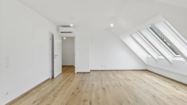 Helles Dachgeschosszimmer mit Holzboden, Dachfenstern und Klimaanlage in einem Neubau.