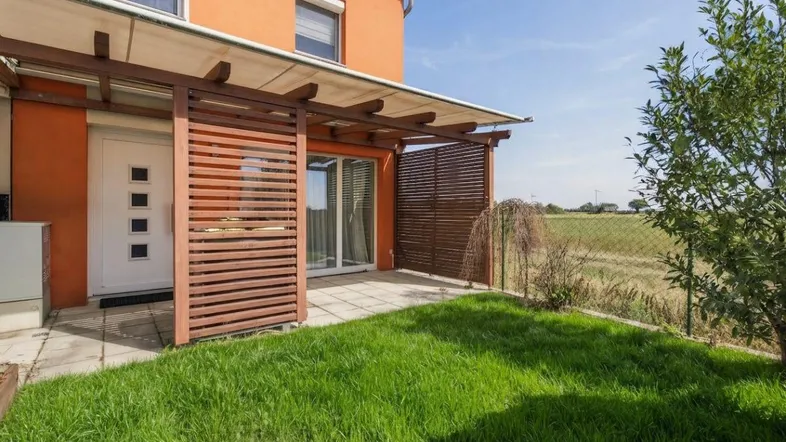 Überdachte Terrasse mit Holzlamellen und Blick ins Grüne, angrenzend an einen kleinen Rasenbereich.