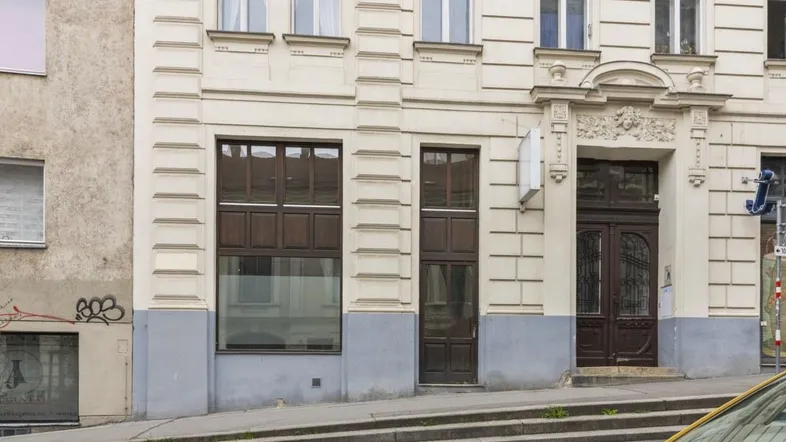 Nahaufnahme der Fassade eines Altbaus mit großen Fenstern und einem verzierten Eingangsbereich auf Straßenniveau.