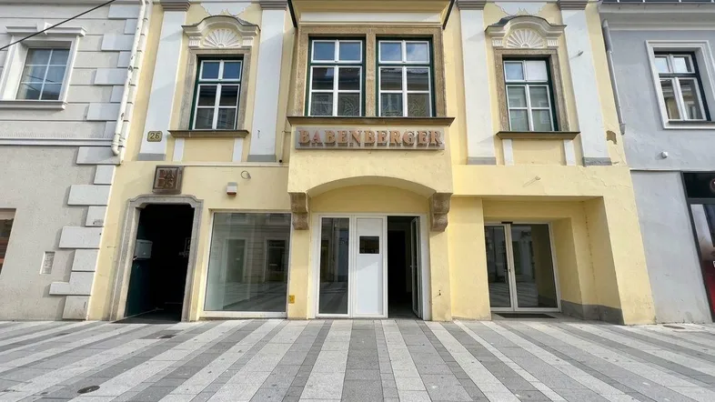 Historisches Gebäude mit gelber Fassade und Geschäftsräumen im Erdgeschoss an einer Straße.