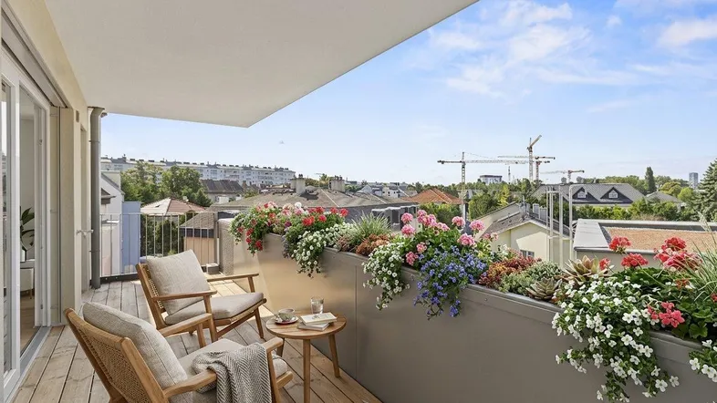 Möblierter Balkon mit Holzboden, Blumenkästen und weitem Blick über die Stadt.