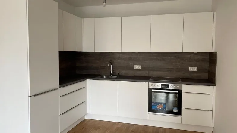 Moderne Einbauküche mit weißen Schränken, dunkler Arbeitsplatte und Holzfußboden.