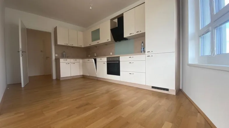 Moderne Einbauküche mit hellen Schränken und Holzparkettboden in einem offenen Wohnbereich.