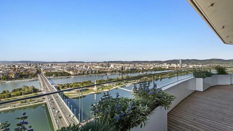 Großer Balkon mit Holzboden, Glasgeländer und weitem Blick über die Stadt und den Fluss.