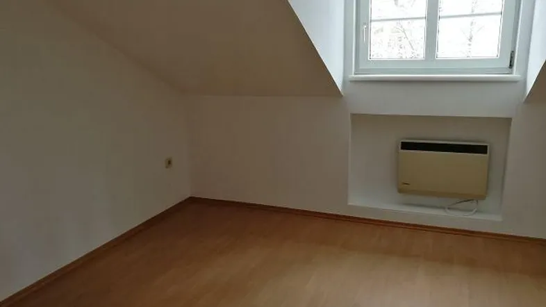 Leerer Raum mit Dachschräge, Fenster und hellem Laminatboden.