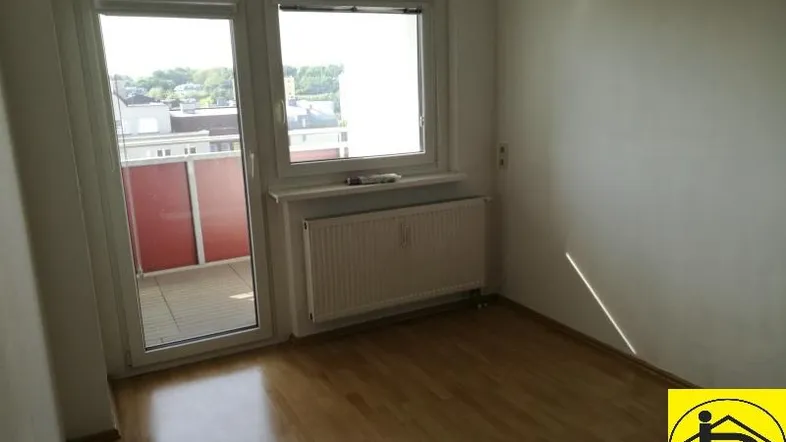 Helles Zimmer mit Holzboden und Zugang zu einem kleinen Balkon, ideal als Schlafzimmer.