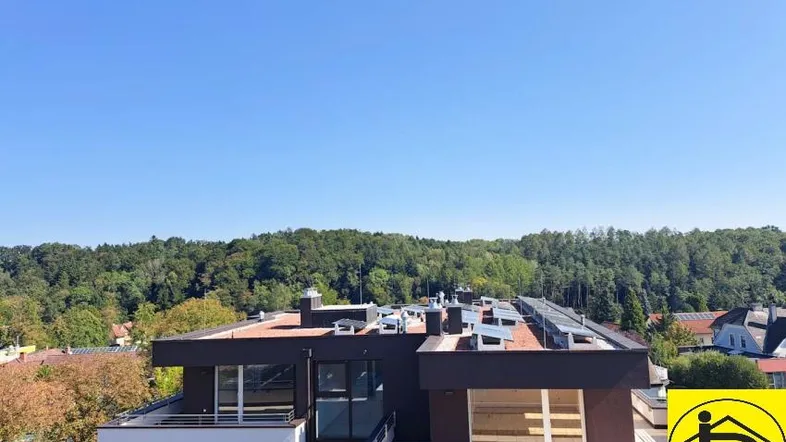 Moderne Wohnanlage mit Flachdach und Photovoltaikanlage, umgeben von viel Grün und weitem Himmel.