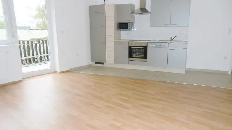 Heller Wohn- und Essbereich mit integrierter Küche, Laminatboden und Zugang zum Balkon.