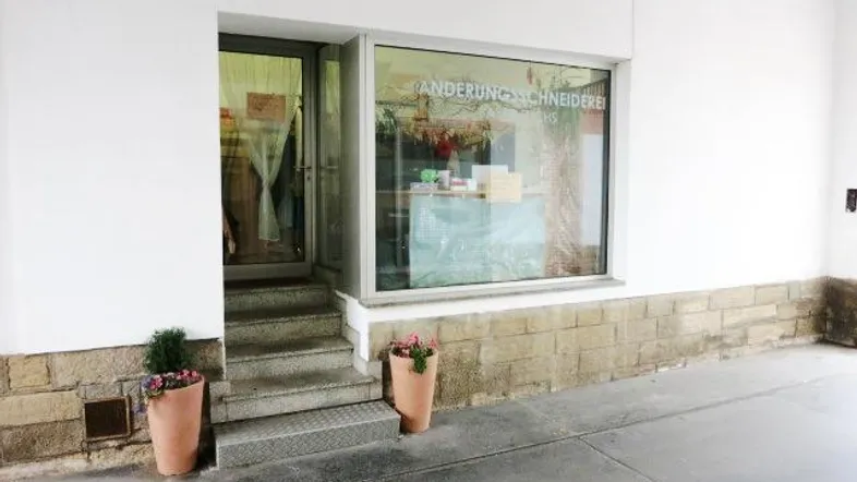 Außenansicht eines Ladenlokals mit Schaufenster und Eingangstür, umgeben von einer weißen Fassade und Steinverkleidung.