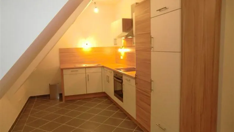 Moderne Einbauküche im Dachgeschoss mit hellen Fronten, Fliesenboden und schräger Decke.