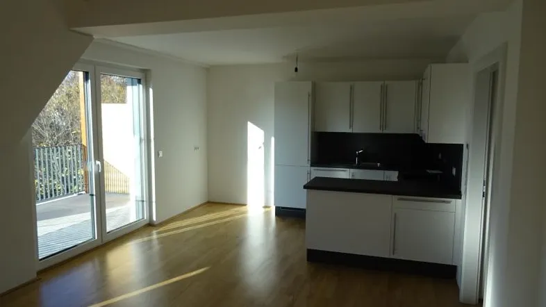 Heller offener Wohnbereich mit integrierter Küche, Parkettboden und Zugang zu einem Balkon.