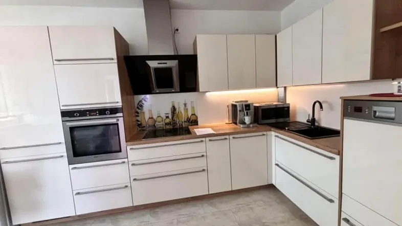 Moderne Küche mit weißen Hochglanzfronten, Holzarbeitsplatte und integrierten Geräten für effizientes Kochen.