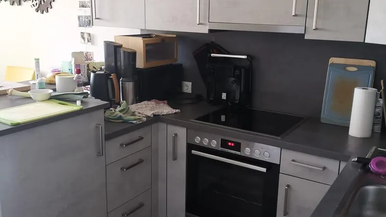 Moderne Küche mit grauen Schränken, integriertem Backofen, Kochfeld und Laminatboden.