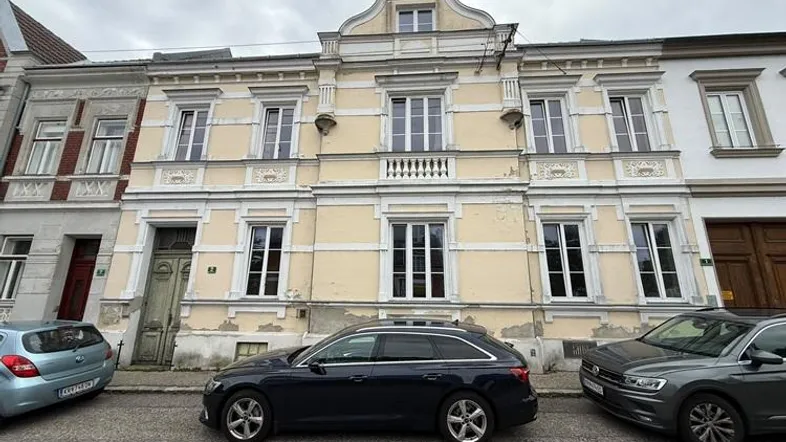Historisches Gebäude mit verzierter Fassade und parkenden Autos auf der Straße.