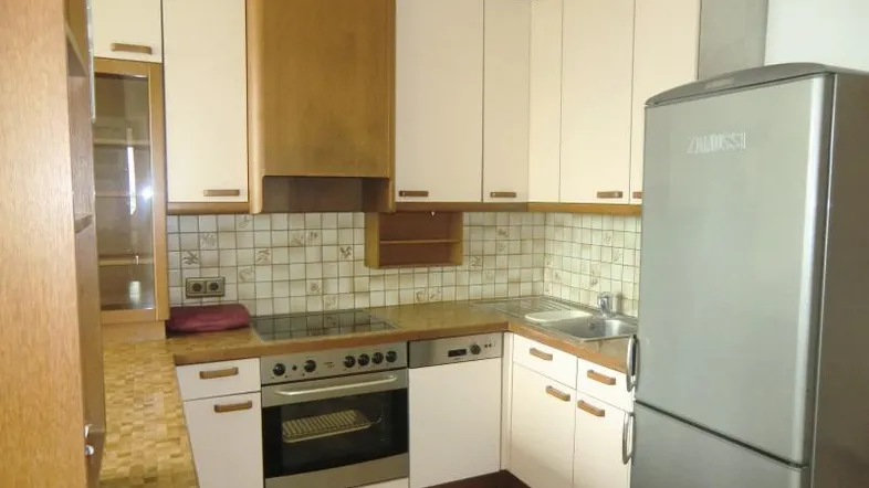 Funktionale Küche mit hellen Schränken, Fliesenboden und integrierten Geräten, inklusive Kühlschrank.