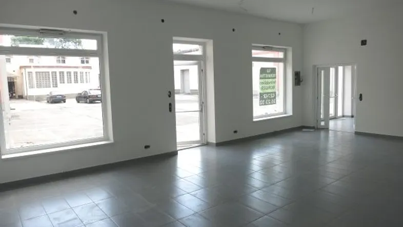 Geräumiger, leerer Innenraum mit großen Fenstern und Fliesenboden, ideal für gewerbliche Nutzung.