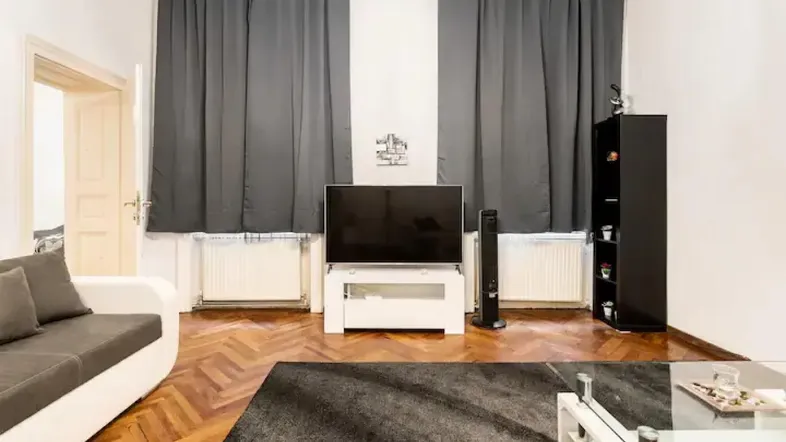 Helles Wohnzimmer mit Parkettboden, Fernseher und dunklen Vorhängen, ausgestattet mit einem Teppich.
