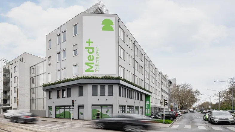 Modernes Eckgebäude mit großen Fenstern und grüner Beschilderung an einer belebten Straße.