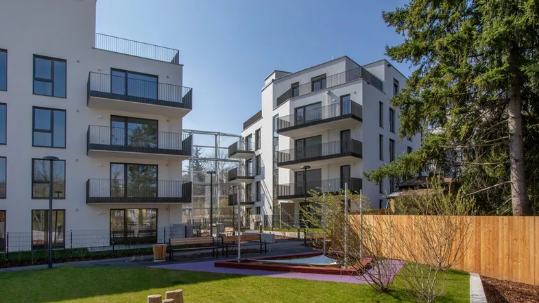 Moderne Wohngebäude mit Balkonen und einem gemeinschaftlichen Gartenbereich inklusive Spielplatz für Kinder.