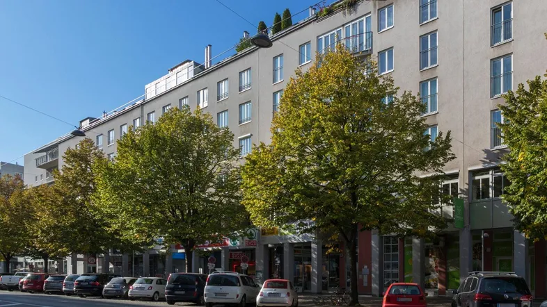 Mehrstöckiges Wohngebäude mit Geschäften im Erdgeschoss und Bäumen entlang der Straße.