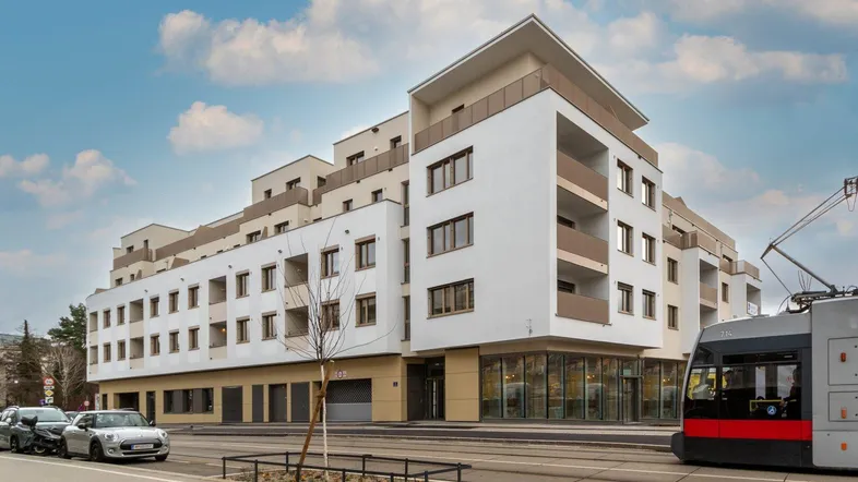 Modernes Wohngebäude mit weißer Fassade, großen Fenstern und Balkonen an einer belebten Straße.