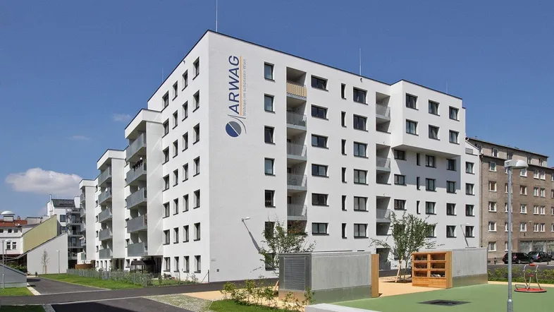 Modernes Wohngebäude mit weißer Fassade, Balkonen und einem Spielplatz im Außenbereich.