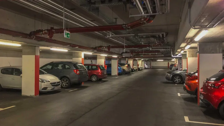 Geräumige Tiefgarage mit vielen Stellplätzen und sichtbaren Installationen an der Decke.