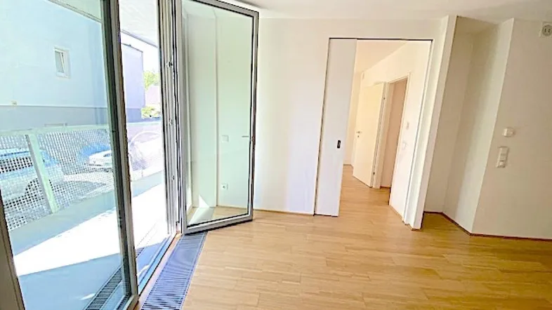 Heller Wohnraum mit Parkettboden und Zugang zu einem großen Balkon durch Falttüren.