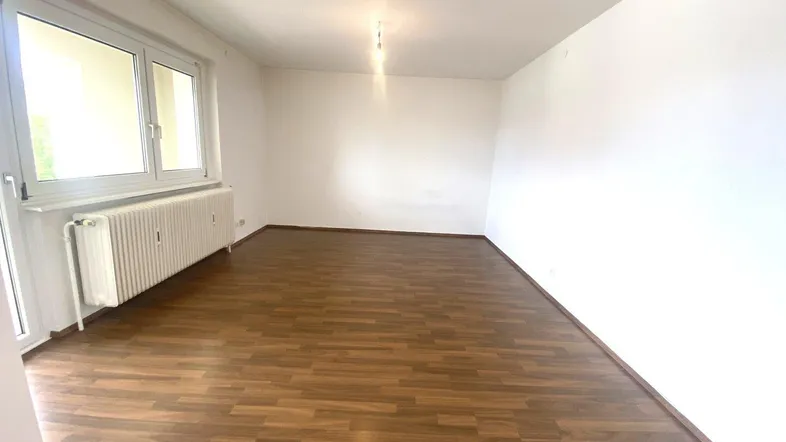 Helles, leeres Zimmer mit Laminatboden und großem Fenster, bereit zur individuellen Gestaltung.
