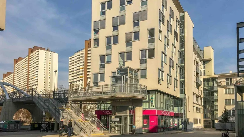 Modernes Gebäude mit heller Fassade, vielen Fenstern und einem externen Glasaufzug.