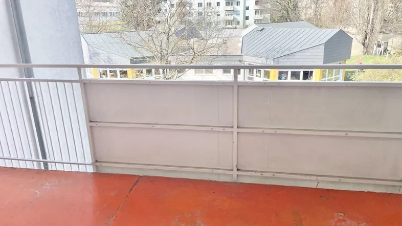 Balkon mit rotem Boden und Blick auf umliegende Gebäude und Bäume.