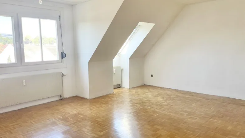 Helles Zimmer im Dachgeschoss mit Parkettboden, Dachschrägen und einem Dachfenster.
