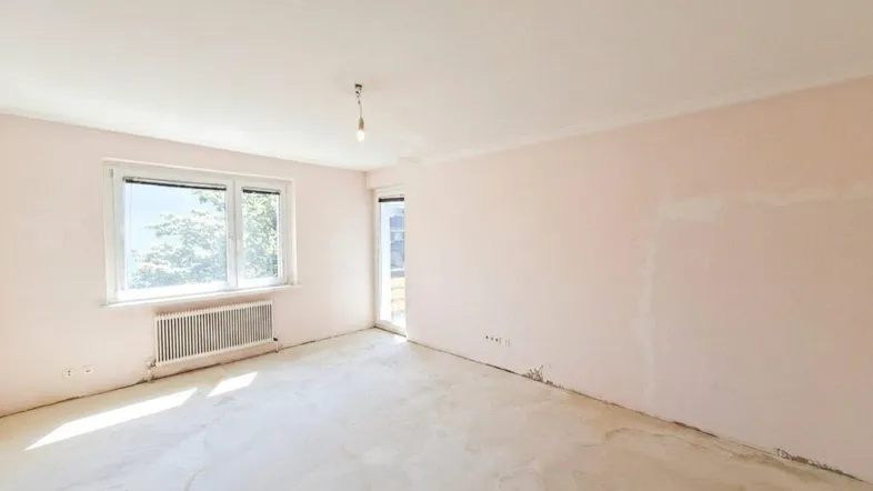 Helles, unmöbliertes Zimmer mit rosa Wänden, Betonboden und Zugang zum Balkon.