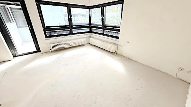 Heller Raum mit großen Fenstern, Heizkörpern und Zugang zu einem Balkon, bereit für die Gestaltung.