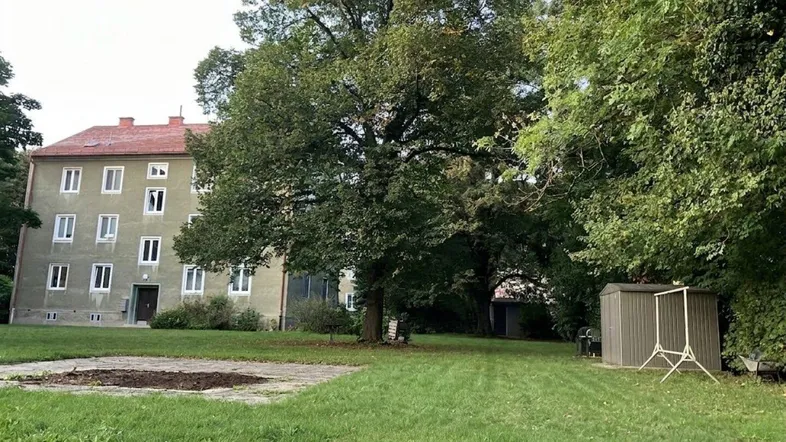 Mehrfamilienhaus mit grüner Fassade, umgeben von einem großen Garten und alten Bäumen.