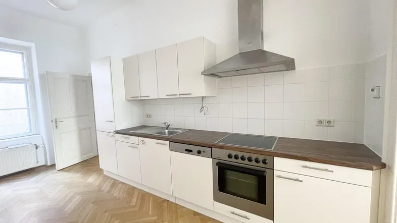 Helle Küche mit weißen Schränken, Holzarbeitsplatte und Fischgrätparkettboden, ausgestattet mit modernen Geräten.