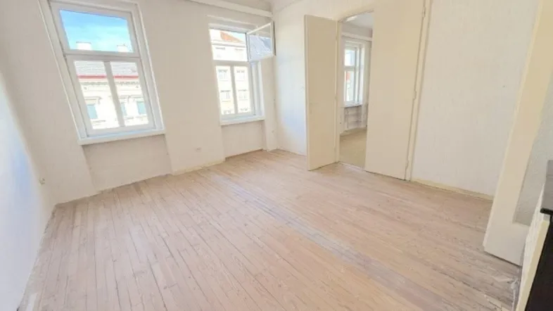 Helles Zimmer mit abgezogenen Holzdielen und Blick auf die Straße, bereit zur Renovierung.
