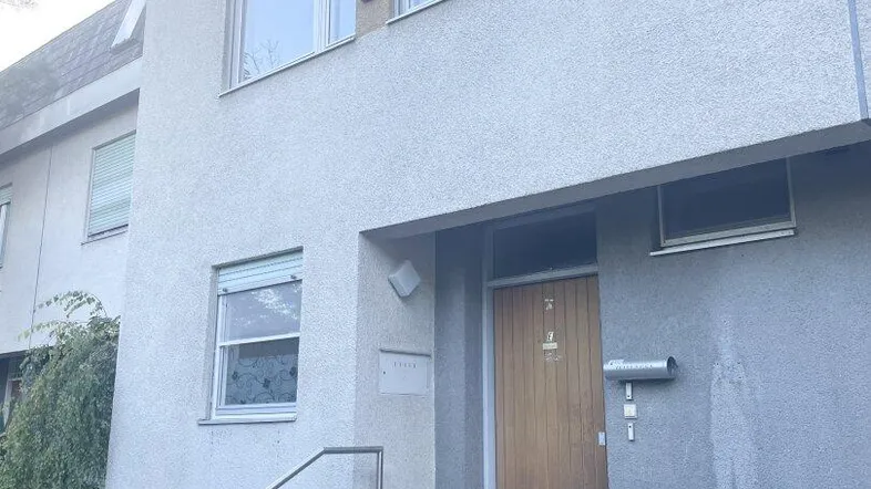 Eingangsbereich eines Hauses mit Holzhaustür, Treppe und Fenstern mit Rollläden.