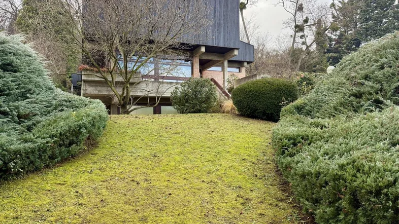 Modernes Haus mit dunkler Holzfassade, umgeben von einem gepflegten Garten und Bäumen.