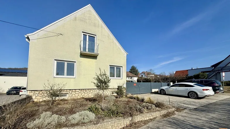 Helles Einfamilienhaus mit gelber Fassade, kleinem Vorgarten und Stellplätzen im Freien.