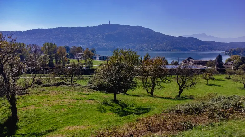 Weitläufige grüne Landschaft mit See und Bergen im Hintergrund unter blauem Himmel.