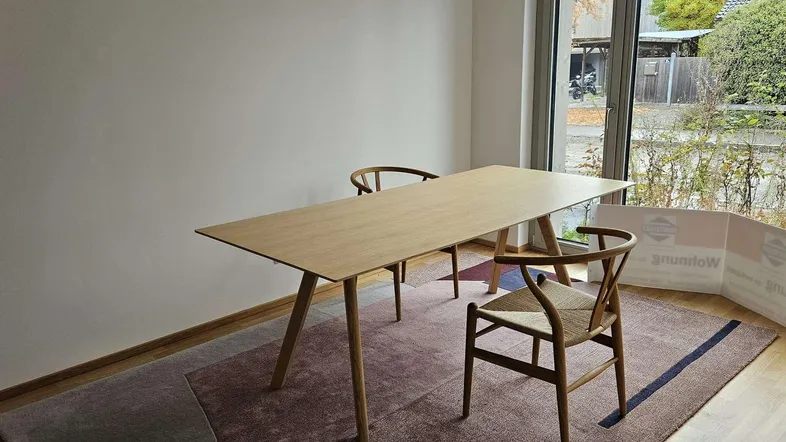 Heller Essbereich mit modernem Holztisch und Stühlen, große Fenster bieten Blick ins Grüne.