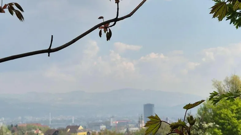 Panoramablick über eine grüne Hügellandschaft mit einer Stadt und Bergen im Hintergrund.