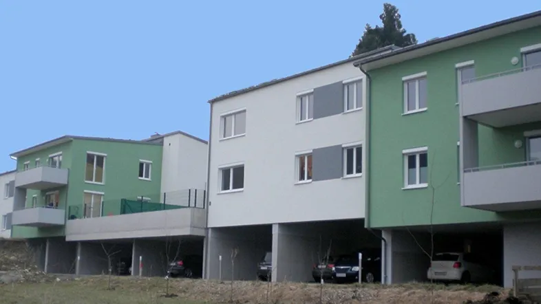 Mehrere moderne Wohngebäude mit grünen und weißen Fassaden sowie überdachten Parkplätzen im Erdgeschoss.