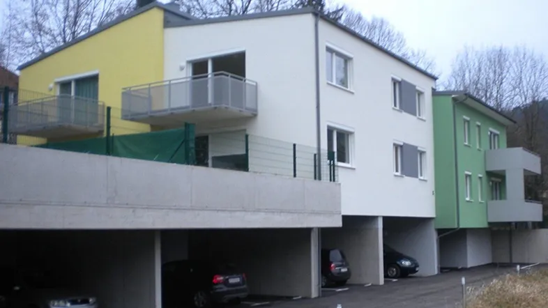 Moderne Mehrfamilienhäuser mit farbigen Fassaden und integrierten Carports im Erdgeschoss.