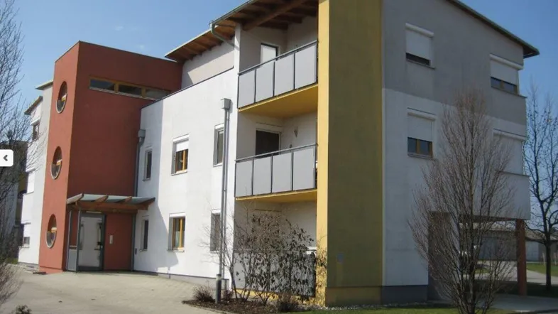 Modernes Mehrfamilienhaus mit farbiger Fassade, Balkonen und gepflegter Außenanlage unter blauem Himmel.