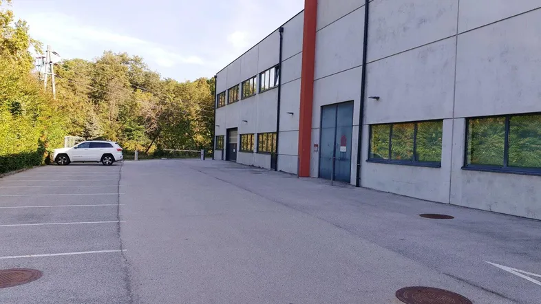 Gebäudeaußenansicht mit großem Parkplatz und umgebender Natur, ideal für gewerbliche Nutzung.